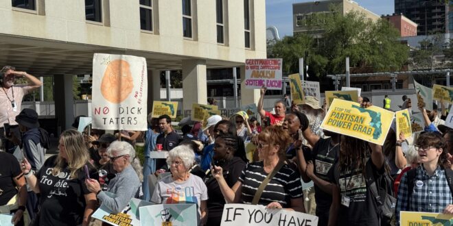 Crowd of protesters holding colorful signs in an urban plaza, many signs advocating against partisan power grabs and voting maps reform.