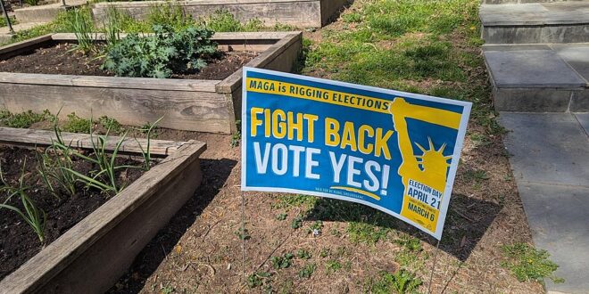 Campaign sign in a front yard: 'FIGHT BACK VOTE YES!' with Statue of Liberty graphic and election date info.
