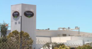 Taylor Farms facility sign on a tall corrugated metal tower against a blue sky.