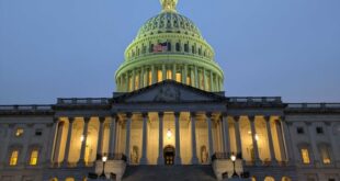 Front view of the U.S. Capitol at dusk, dome lit with a flag visible, grand staircase and columns in the foreground.