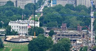 Aerial view of the White House grounds with a construction site and tall crane to the right, surrounded by trees and city buildings.