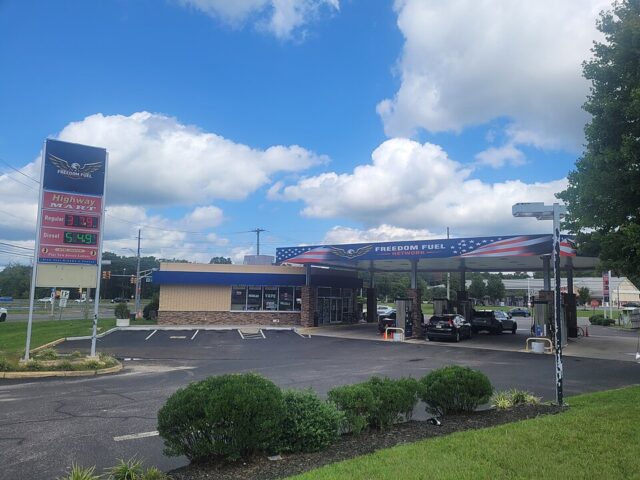 Freedom_Fuel_Network_gas_station_in_Egg_Harbor_Township_New_Jersey_August_2026 - Poli Alert Freedom Fuel gas station with a blue, flag-themed canopy and cars fueling under a sunny, partly cloudy sky.