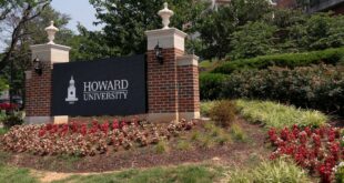 Howard University entrance sign flanked by brick pillars, lanterns, and blooming flower beds in a landscaped campus entrance.