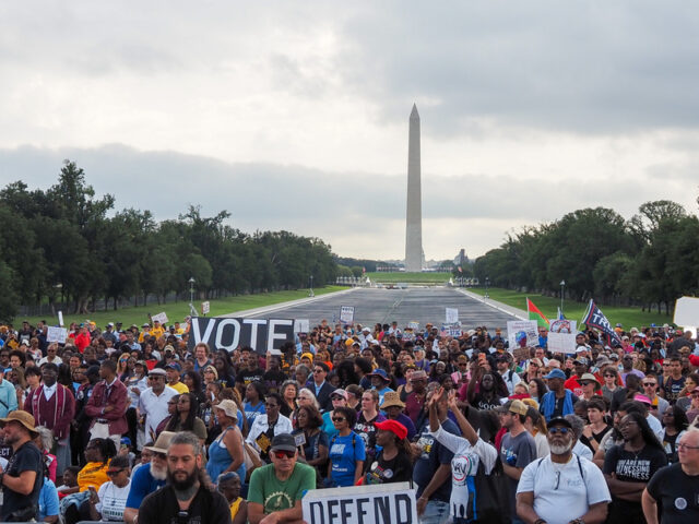 March on Washington - Poli Alert Crowd of protesters on the National Mall near the Washington Monument, holding large signs that read VOTE and DEFEND.